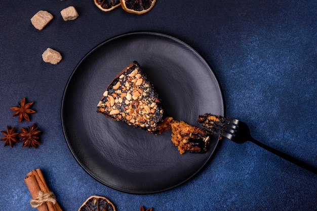 A piece of fresh delicious cake with nuts and chocolate on a black plate against a dark blue background