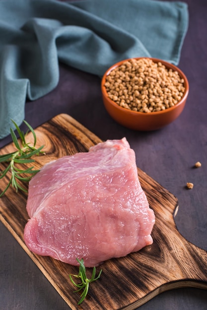 A piece of fresh meat on a cutting board and soy mince in a bowl on the table vertical view