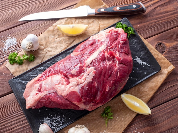 A piece of fresh raw beef lies on parchment surrounded by spices herbs and vegetables The knife is lying nearby Top view flat lay Food composition