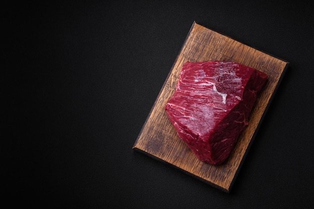 A piece of fresh raw beef with salt spices and herbs on a wooden cutting board