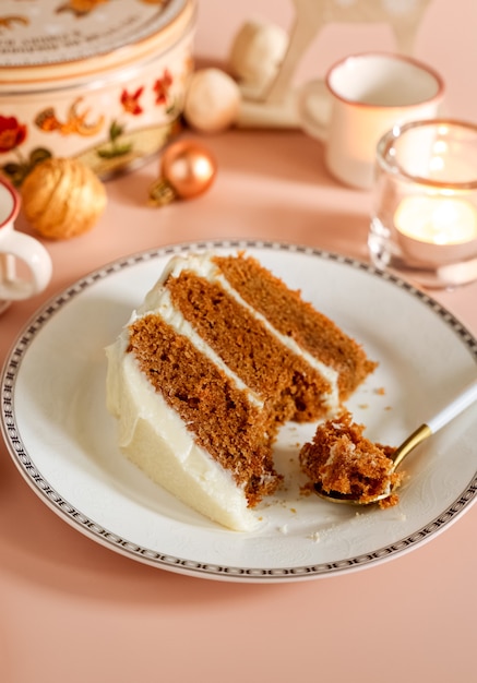 Piece of glazed carrot layer cake on white plate with Christmas seasonal background.