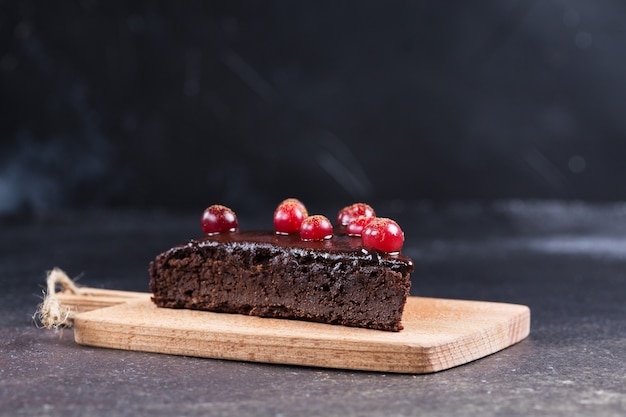 A piece of gluten-free chocolate cake decorated with cranberries on the kitchen board, on a black blurred background. Healthy eating.