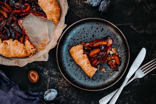 A piece of homemade plum pie on a black plate