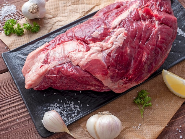 A piece of marbled beef lies on parchment surrounded by herbs, garlic, salt. Top view, flat lay. food composition