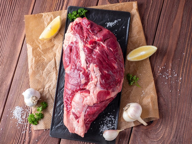 A piece of marbled beef lies on parchment surrounded by herbs, garlic, salt. Top view, flat lay. food composition