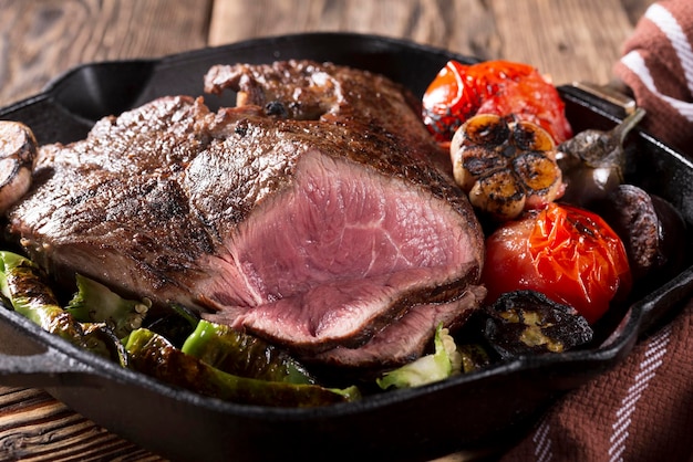 A piece of meat grilled in a castiron pan with vegetables closeup