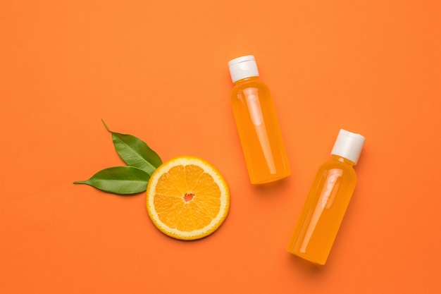 A piece of orange with leaves and two bottles of juice on an orange background. Flat lay.