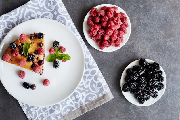 Piece of pie with blueberries, raspberry and mint for dessert on a white plate, napkin. Pieces of delicious homemade cake on a table