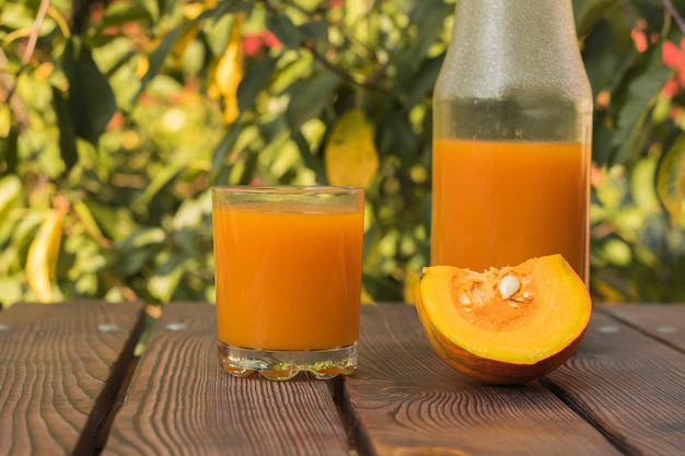 A piece of pumpkin a glass and a bottle of pumpkin juice