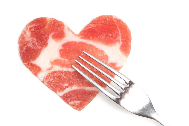 A piece of raw meat in the form of heart and a silver fork Isolated