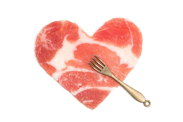 A piece of raw meat in the form of a heart and a small fork Isolated