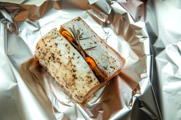 Piece of raw meat with rosemary and dried apricots in foil ready to cook.