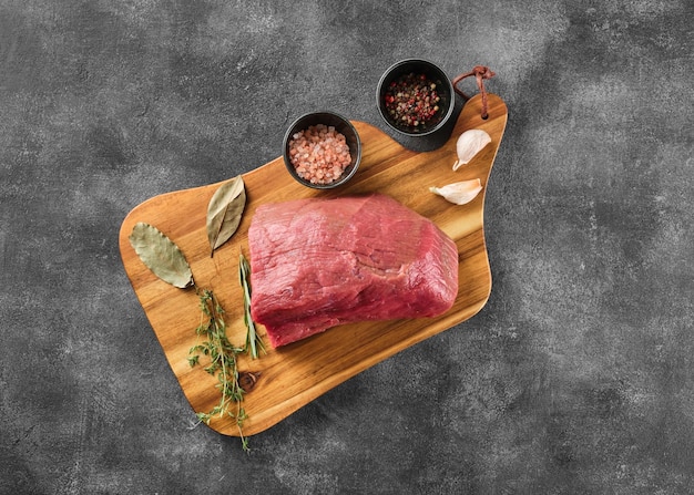 Piece of raw rump steak prepared with spices on wooden board over grey background