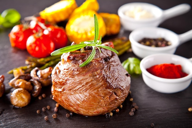 Piece of red meat steak with rosemary served on black stone surface