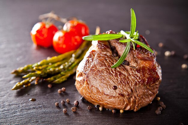 Piece of red meat steak with rosemary served on black stone surface