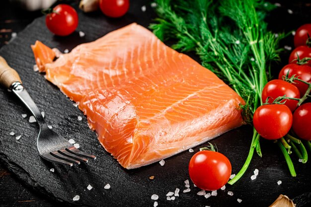 A piece of salted salmon with tomatoes and greens on a stone board