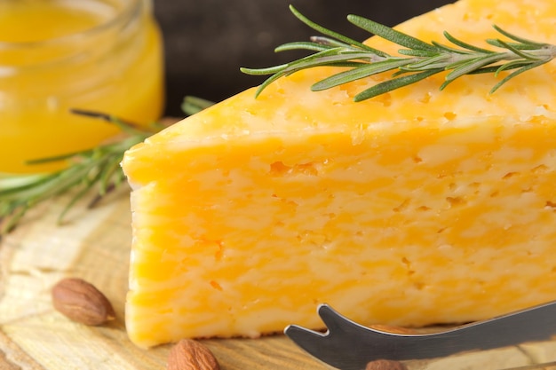 A piece of tasty marbled cheese on a wooden stand with almonds, rosemary and honey on a dark background. close-up