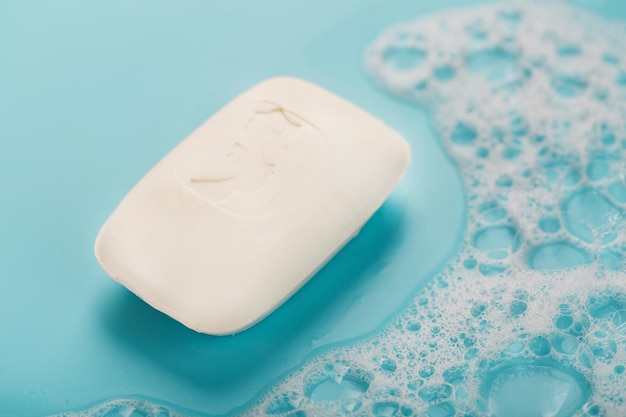 A piece of white soap with foam on blue background Backdrop with copt space