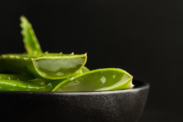 Pieces of aloe vera leaf in a black bowl in a close up view and on a dark background