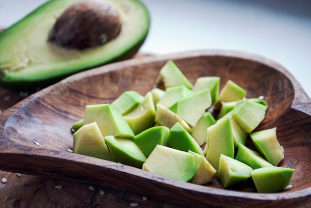 Pieces of avocado in a wooden dish next to half an avocado.