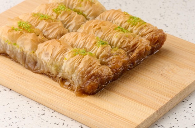 Pieces of baked baklava in honey and sprinkled with pistachios on a wooden board