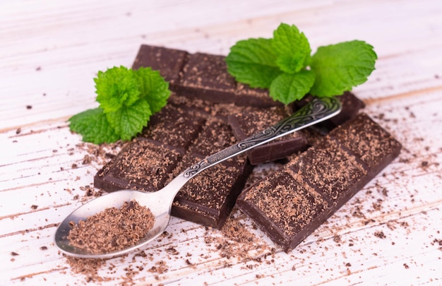 Pieces of dark chocolate with mint leaves on a white wooden background.