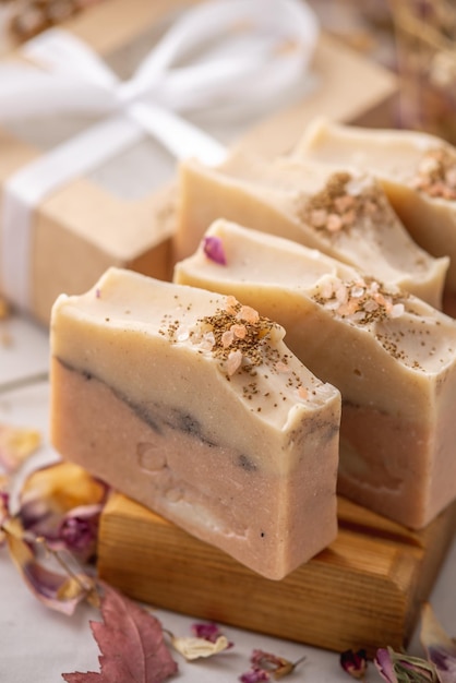 Pieces of delicate fragrant natural handmade soap on a wooden soap dish On the table next to the soap is a gift box with a ribbon and dry flower petals