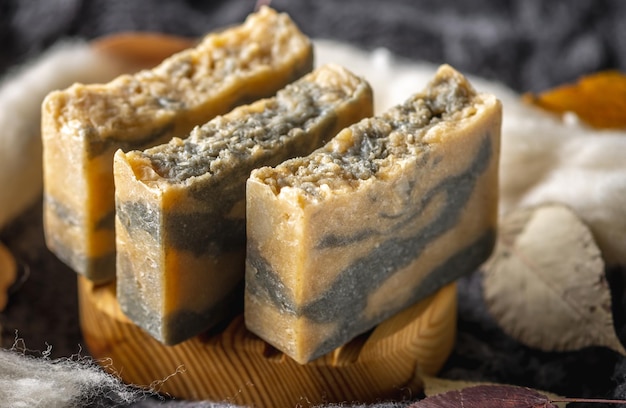 Pieces of handmade natural soap on a wooden soap dish against the background of a warm sweater and dry leaves Concept of a cozy autumn atmosphere organic cosmetics for the skin care