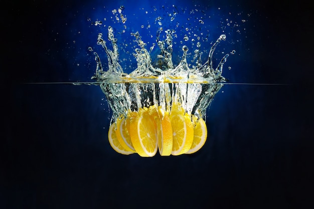 Pieces of lemon thrown into the water against a deep blue background. Underwater shooting.