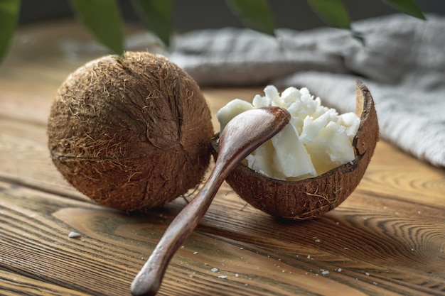 Pieces of organic coconut butter in a bowl spoon and fresh coconut on a wooden table Concept of healthy ingredient for cooking and natural cosmetics