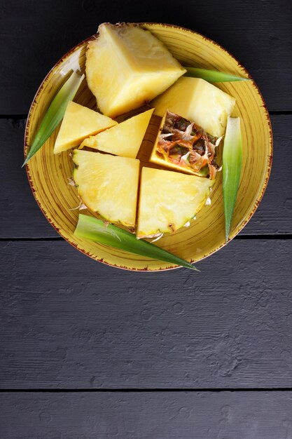 Pieces of pineapple on yellow plate Pineapple fruit with green leaves on dark background Top view Copy space