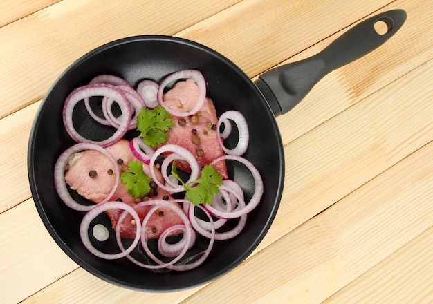 A pieces of pork with onions fried in pan on wooden table