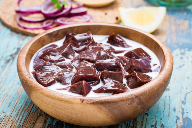 Pieces of raw beef liver soaked in milk in a wooden bowl  on the table