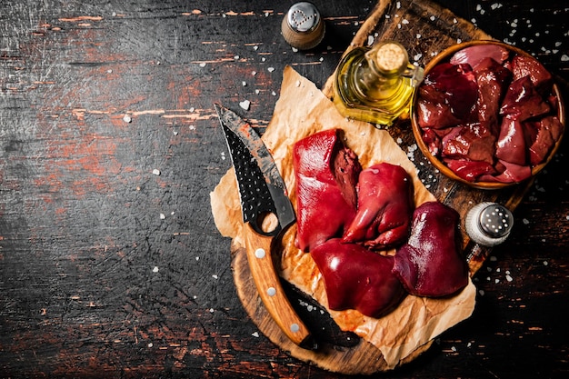 Pieces of raw liver on a cutting board with oil and spices