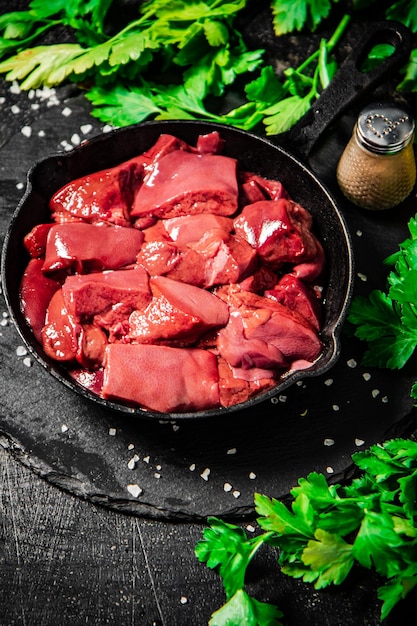 Pieces of raw liver in a frying pan with parsley and spices