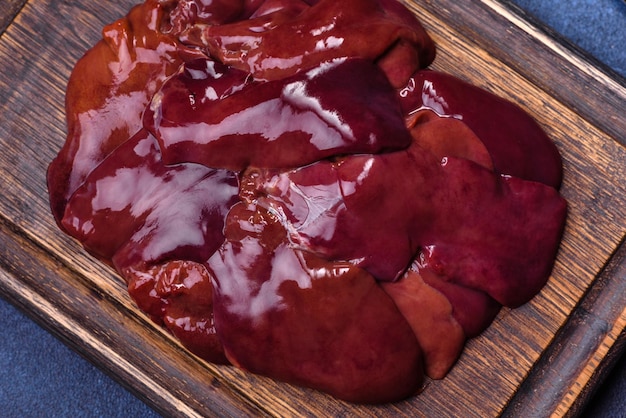 Pieces of raw liver on a wooden cutting board against a dark concrete background