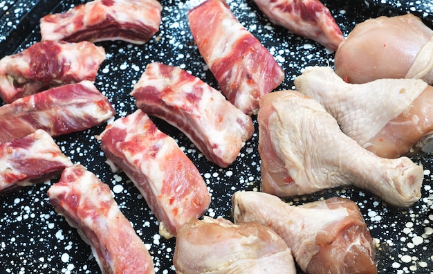 Pieces of raw meat and chicken legs on a baking sheet before cooking