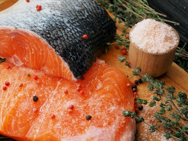 Pieces of raw salmon with herbs salt and pepper Wooden salt shaker with coarse salt View from above