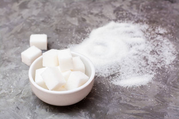 Pieces of refined sugar in a bowl and a pile of sugar sand on the table