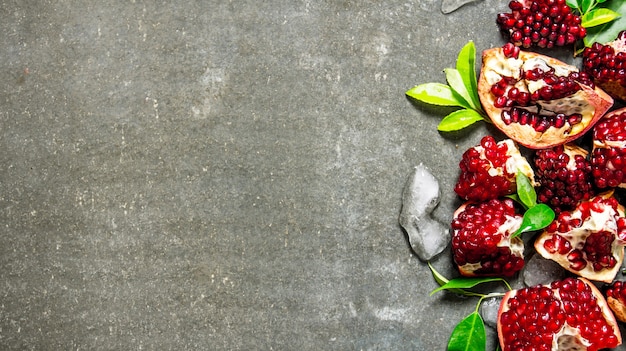 Photo pieces of ripe pomegranate with leaves and ice. on the stone table. free space for text . top view