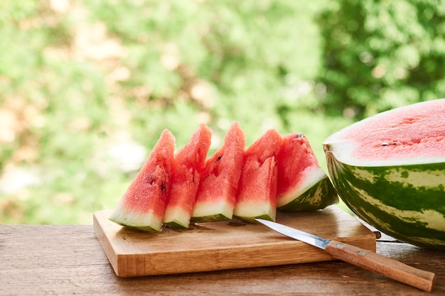 Pieces of ripe red watermelon are on a wooden plank, on green background of foliage. summer food, summer day, summer time