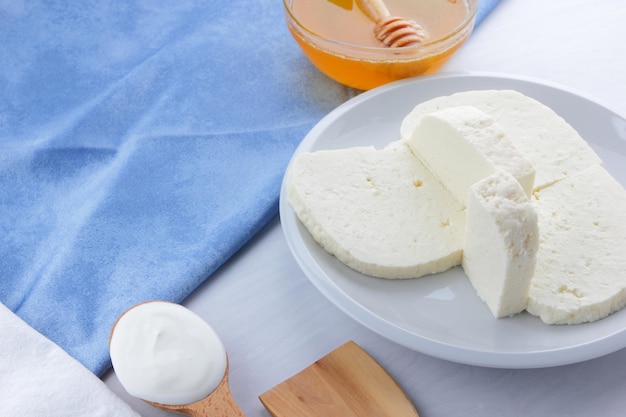 Pieces of soft white brynza on a white plate Cheese with cream and honey on a light background with white and blue napkins Closeup