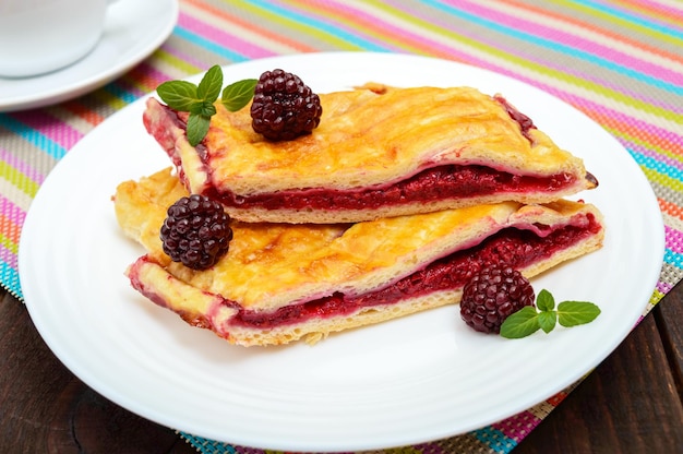 Pieces of sweet berry pie on the white plate and cup of tea on the bright napkin Close up