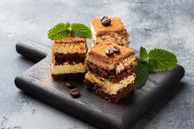 Pieces of tiramisu cake with delicate cream, coffee beans and mint leaves.