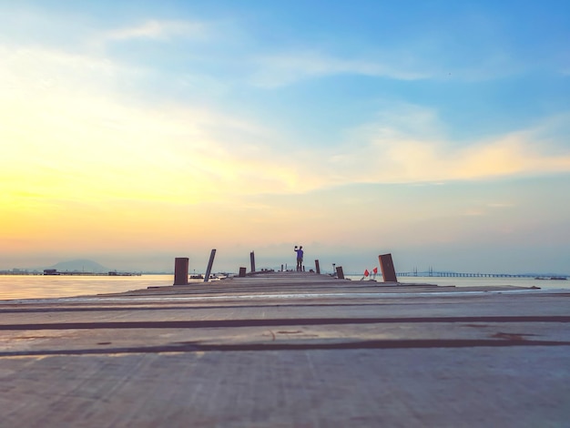 Pier at beach against sky during sunset