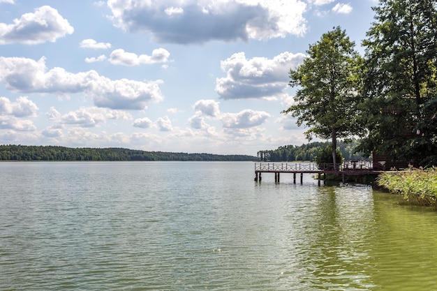 Pier on the shore of a large lake in summer day with beautiful clouds sky reflection