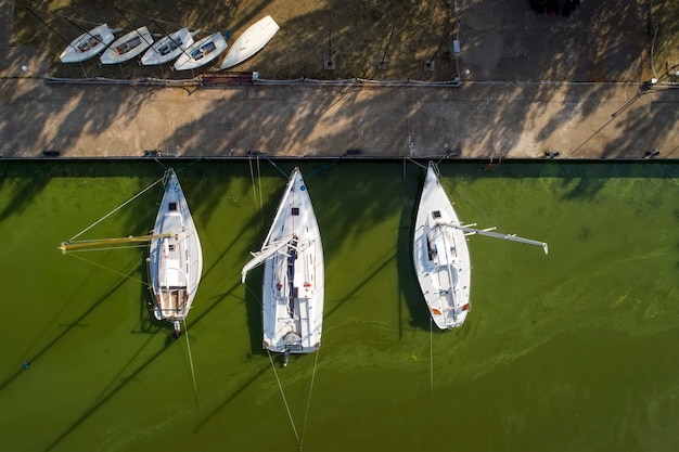 Pier with boats, marina lot. Aerial top view from drone. Green water due to seaweed