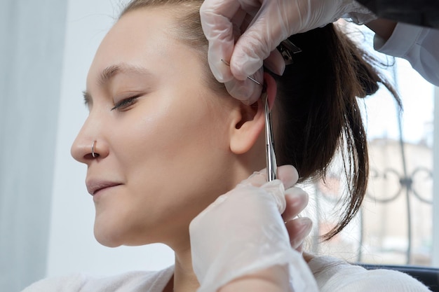 Piercings on an ear Conch and helix piercings close up Professional holding the jewel