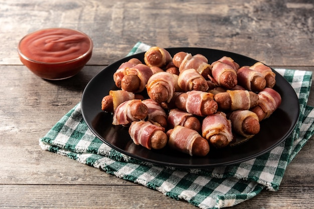 Pig in blankets Sausages wrapped in smoked bacon on wooden table