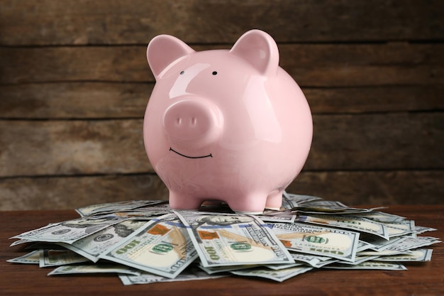 Pig money box and dollar banknotes on wooden wall background